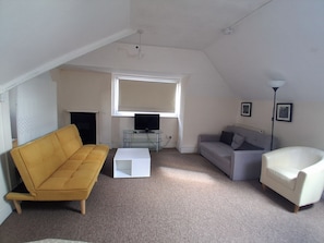 A living room with a yellow sofa, a grey sofa, a white coffee table, and a white armchair. There is a television on a glass table, and two framed pictures on the wall. - Southampton Serenity - 3 Bedroom Apartment (Southampton)