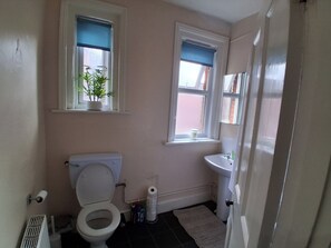 Ein Badezimmer mit Toilette, Waschbecken und zwei Fenstern mit blauen Rollos.