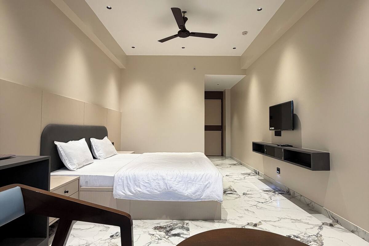 A modern hotel room with a bed, a desk, a chair, a TV, and a ceiling fan.