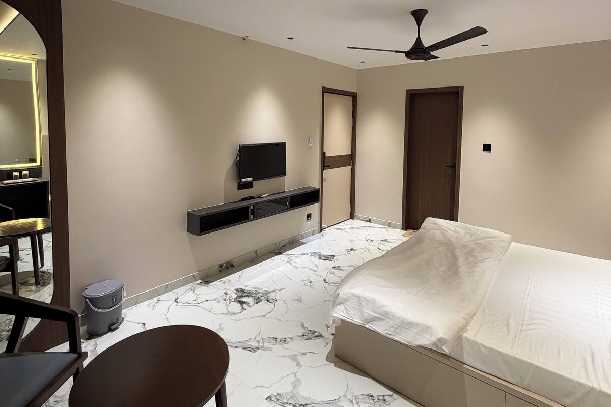 A modern hotel room with a bed, a desk, a chair, a TV, and a ceiling fan.