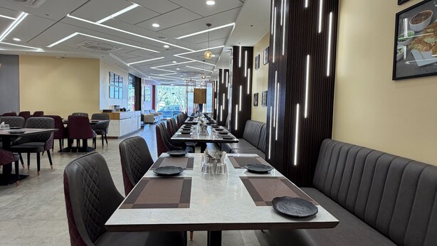 A modern dining area with a long table, cushioned seating, and contemporary lighting. - Bharat Inn Hotel And Restaurant (Nakhtarana)
