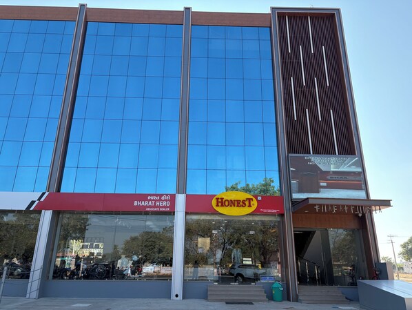 A modern building with a large glass facade, a prominent 'Honest' sign, and a 'Bharat Hero' sign indicating an associate dealership. - Bharat Inn Hotel And Restaurant (Nakhtarana)