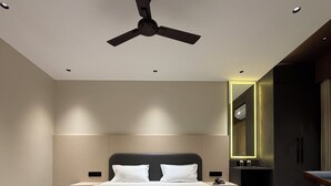 A modern bedroom with a large bed, marble flooring, a ceiling fan, and a mirror with a light. - Bharat Inn Hotel And Restaurant (Nakhtarana)