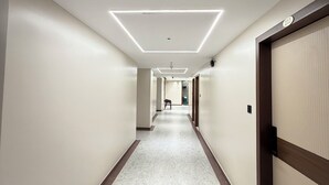 A hotel hallway with a marble floor, recessed lighting, and a door with a number sign. - Bharat Inn Hotel And Restaurant (Nakhtarana)