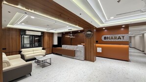 A modern hotel lobby with a reception desk, a sofa, and a ceiling fan. - Bharat Inn Hotel And Restaurant (Nakhtarana)