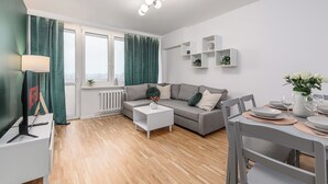 A modern living room with a grey sofa, white coffee table, and a dining table set for four. - Lumina 3-room apartment with balcony (Warsaw)