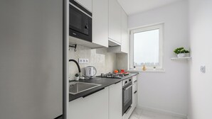 A modern kitchen with white cabinetry, a black countertop, a built-in oven, and a window with a view. - Lumina 3-room apartment with balcony (Warsaw)