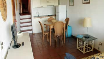 A compact living space with a kitchenette, dining area, and a small side table with a lamp.