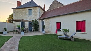 A stone house with a paved patio, a lawn, and a lounge chair. - La Maison des Oiseaux - A room in the heart of the Loire castles. (Crouzilles)
