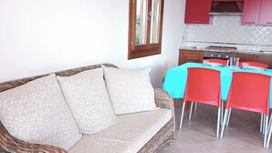 En fletsofa med et mønstret pude, et spisebord med røde stole og et køkken med røde skabe.