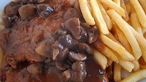 A plate with a breaded cutlet topped with mushrooms and gravy, accompanied by French fries.