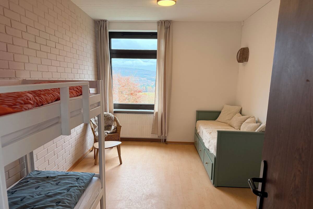 Ein Zimmer mit Etagenbett, einem Einzelbett, einem Stuhl und einem Fenster mit Blick.