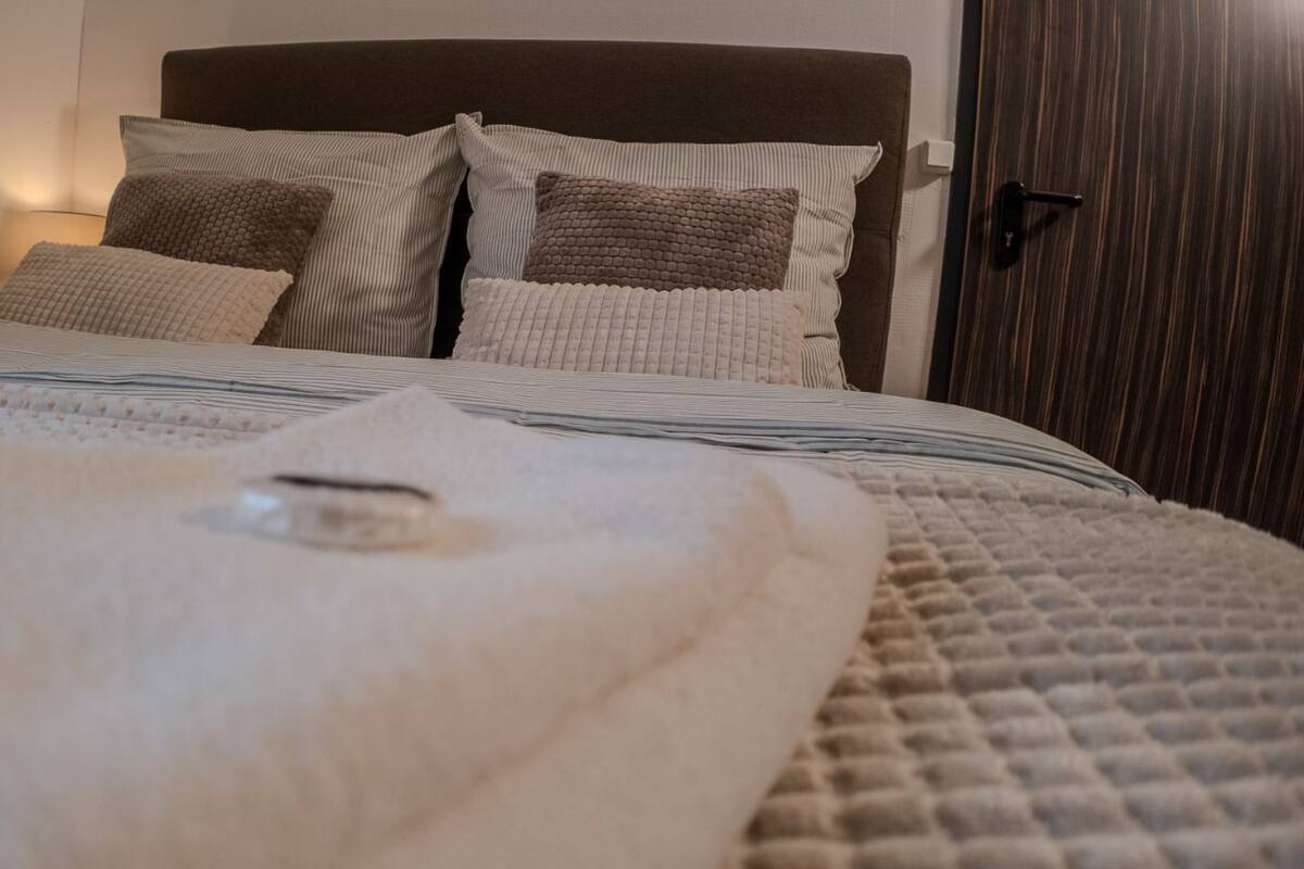 Ein ordentlich gemachtes Bett mit gestreifter Decke und Kissen, einer Nachttischlampe und einer Holztür.