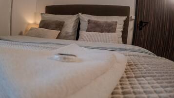 Una cama bien hecha con una colcha y almohadas a rayas, una lámpara de noche y una puerta de madera.