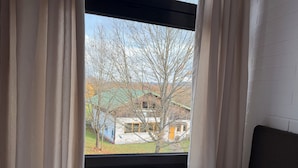 A bedroom with a window, curtains, and a view of a house with a tree.