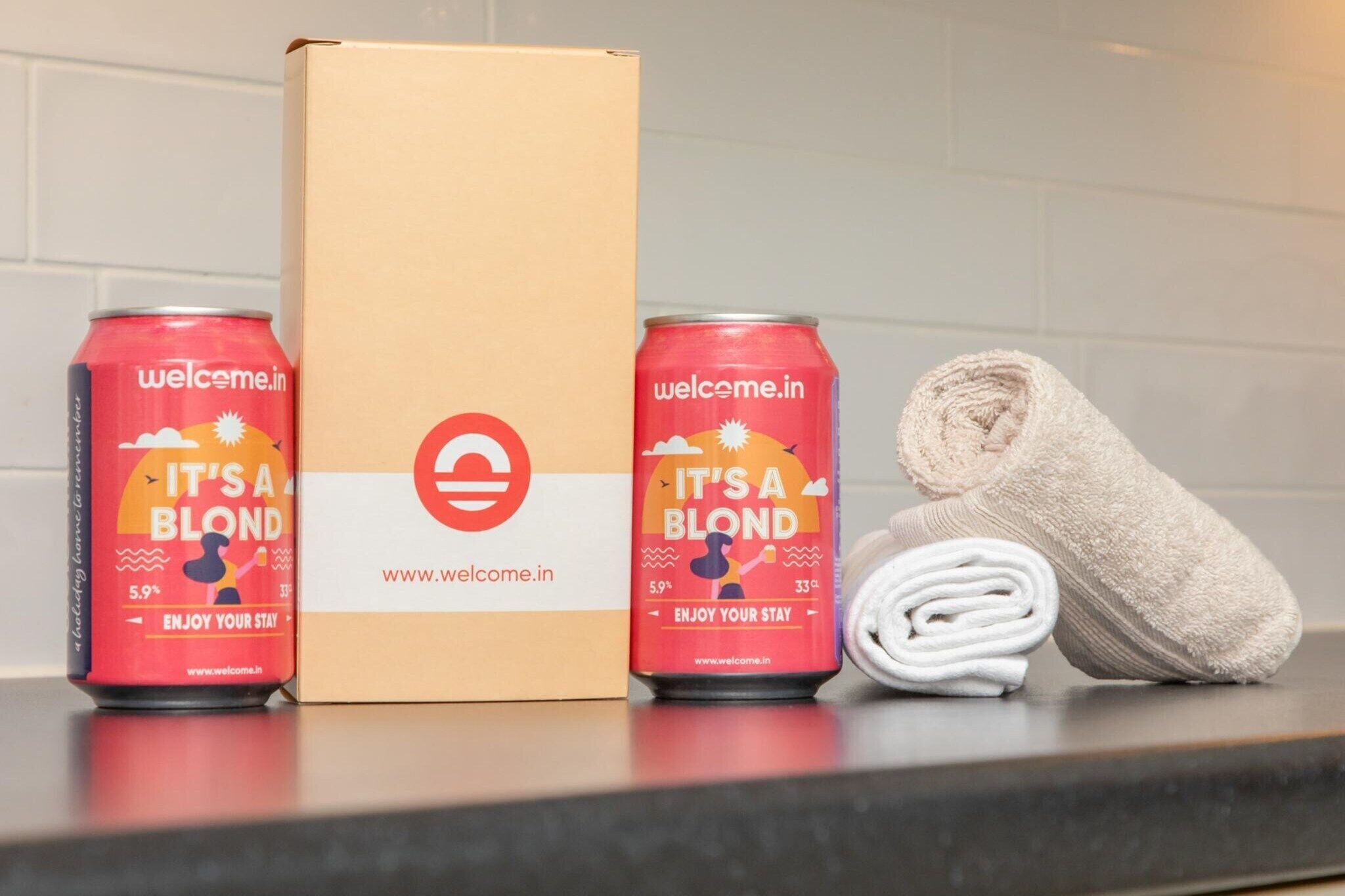 Une boîte en carton, deux canettes de boisson et une serviette enroulée sur un comptoir.