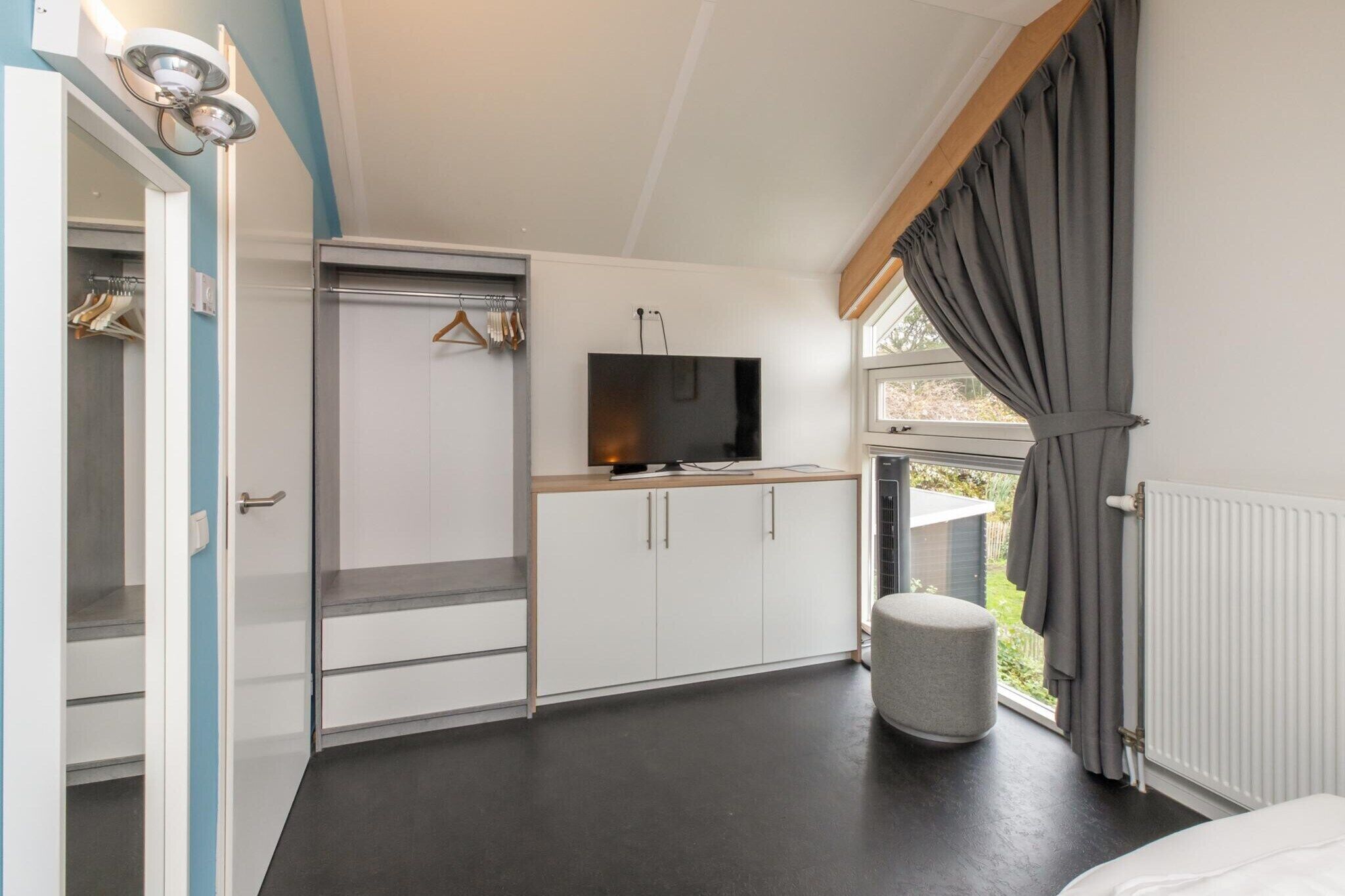 Een slaapkamer met een kledingkast, een televisie, een radiator en een raam met gordijnen.