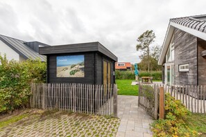 A modern building with a wooden fence, a paved pathway, and a sign with a landscape image. - 6-Person Holiday Home in Renesse (Renesse)