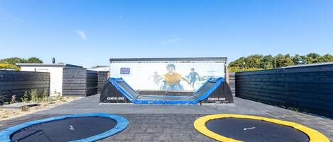 An outdoor trampoline area with two trampolines, one blue and one yellow, and a large inflatable slide.