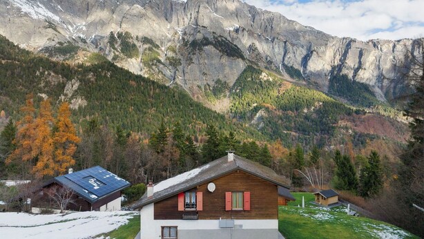 Un rifugio di montagna con tetto spiovente, facciata in legno e un piccolo garage adiacente.