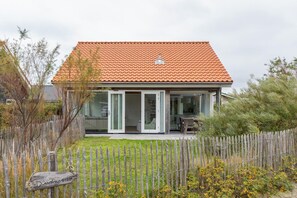 A house with a tiled roof, a fenced yard, and a wooden sign. - Beachside Modern Holiday Home for 6 (Renesse)