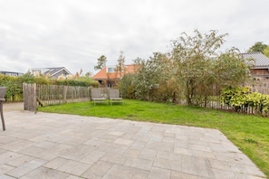 En anlagt terrasse med græsplæne, træhegn og to stole.
