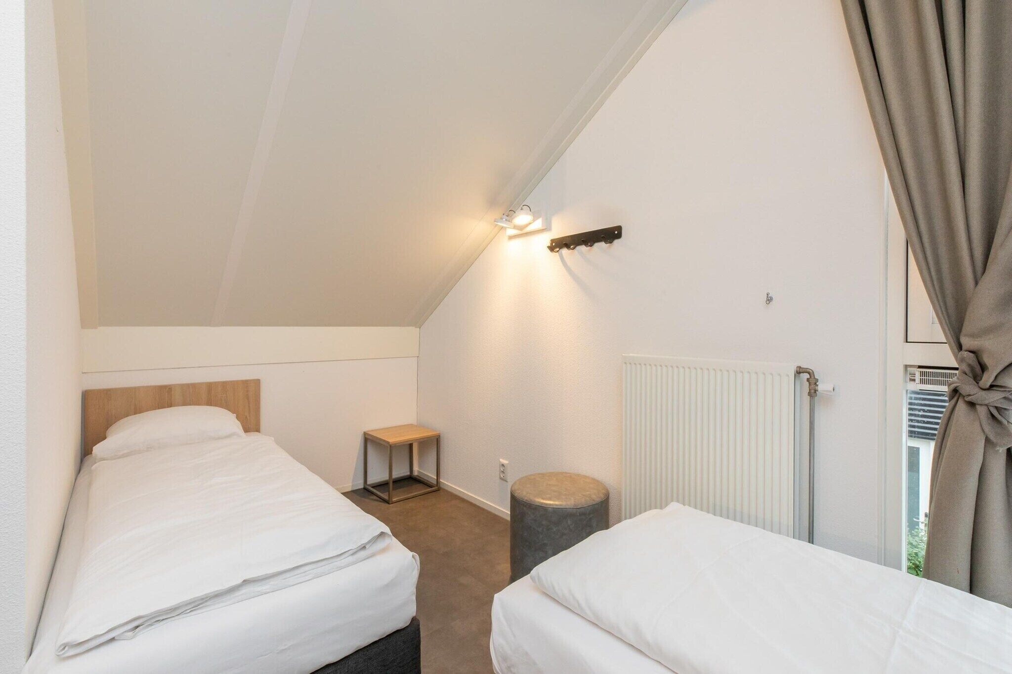 A small, single-room accommodation with two beds, a nightstand, a lamp, and a radiator.