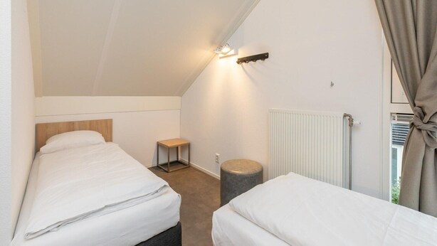 A small, single-room accommodation with two beds, a nightstand, a lamp, and a radiator. - modern comfort, close to the beach. (Renesse)