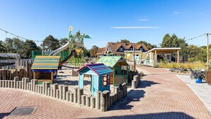 A playground with various play structures, a brick pathway, and buildings in the background. - modern comfort, close to the beach. (Renesse)