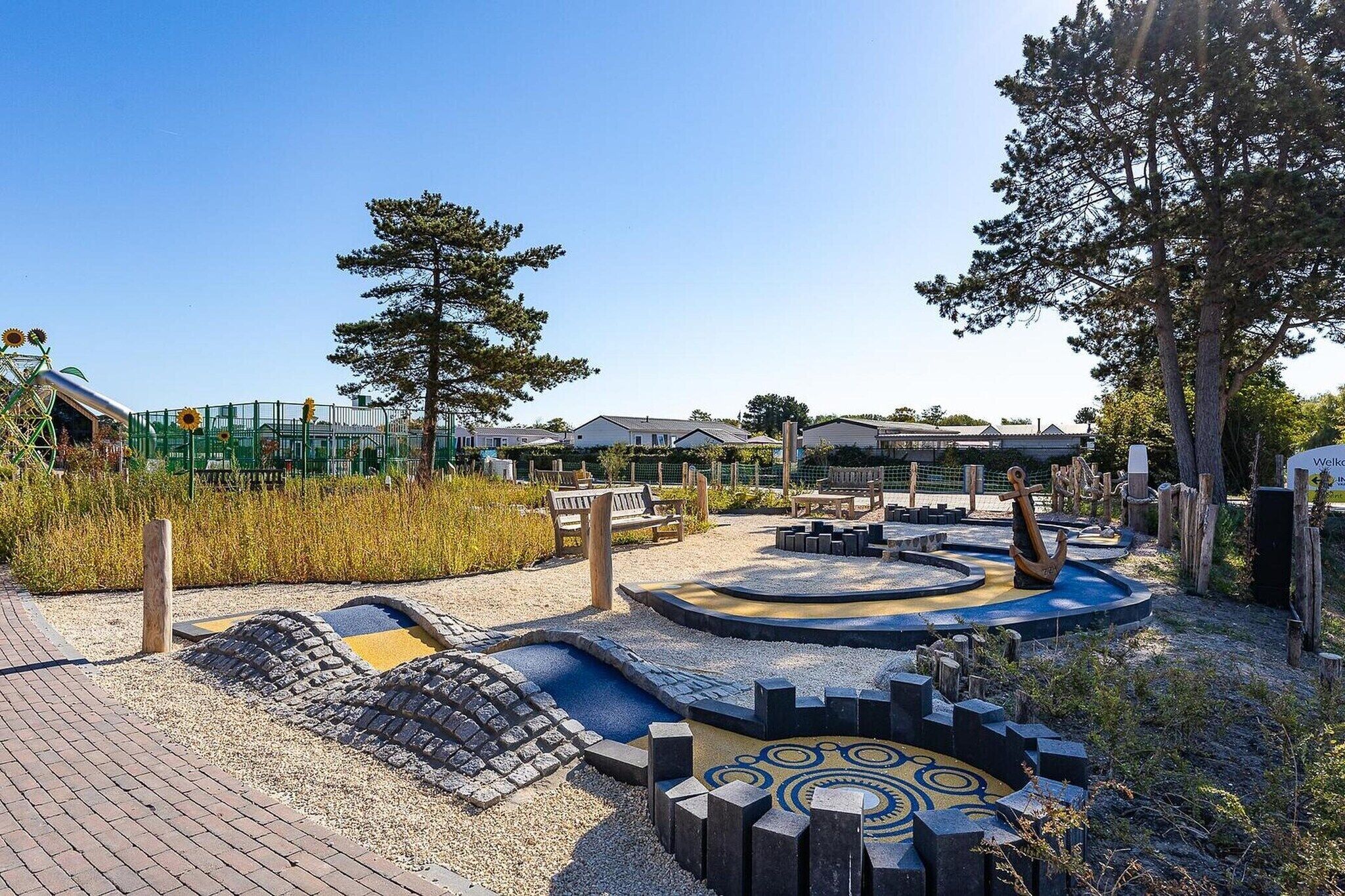 Un parque infantil con una zona de juegos circular, bancos y un jardín cercado.