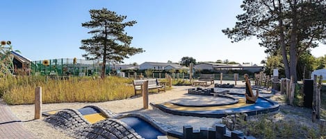 Un parque infantil con una zona de juegos circular, bancos y un jardín cercado.
