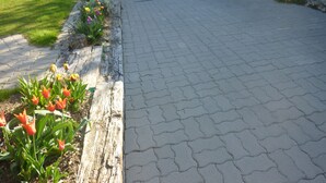 A paved walkway leading to a building entrance, with a flower bed on the left and a stone wall on the right. - Le Gite de Jules at VIGNOT in LORRAINE near VERDUN, NANCY and METZ (Vignot)