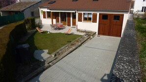 A two-story house with a tiled roof, a front porch with a table and chairs, and a small garden area. - Le Gite de Jules at VIGNOT in LORRAINE near VERDUN, NANCY and METZ (Vignot)
