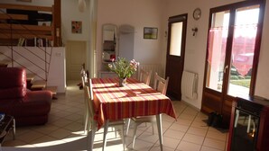 A dining area with a table set for four, a red sofa, a radiator, and a view through a door. - Le Gite de Jules at VIGNOT in LORRAINE near VERDUN, NANCY and METZ (Vignot)