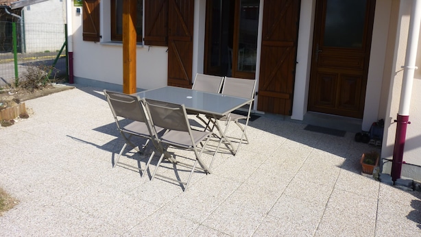 A building with a tiled patio, a table with chairs, wooden doors, and a green sign. - Le Gite de Jules at VIGNOT in LORRAINE near VERDUN, NANCY and METZ (Vignot)