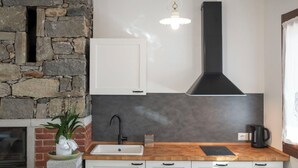 Una cucina con parete in pietra, mobili bianchi, cappa aspirante nera e piano di lavoro in legno.