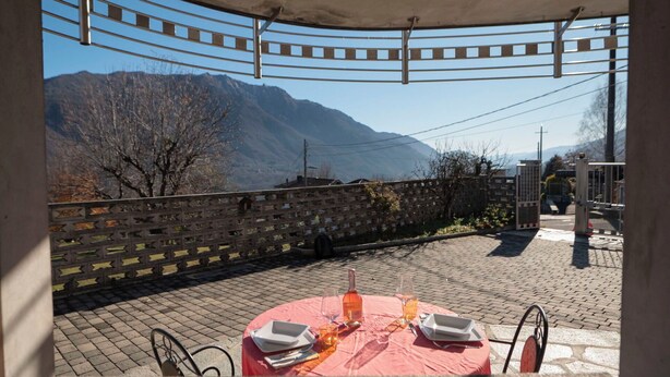 Area pranzo all'aperto con tavolo apparecchiato per due, affacciata su un paesaggio montuoso.