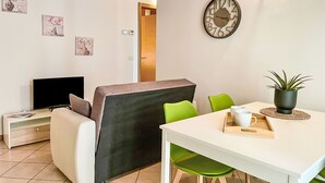 En hyggelig opholdsstue med sofa, fjernsyn, spisebord med stole og et ur på væggen.