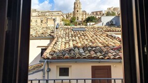 Vista desde una ventana con vistas a un paisaje urbano que destaca una torre de iglesia, tejas de arcilla y edificios circundantes.