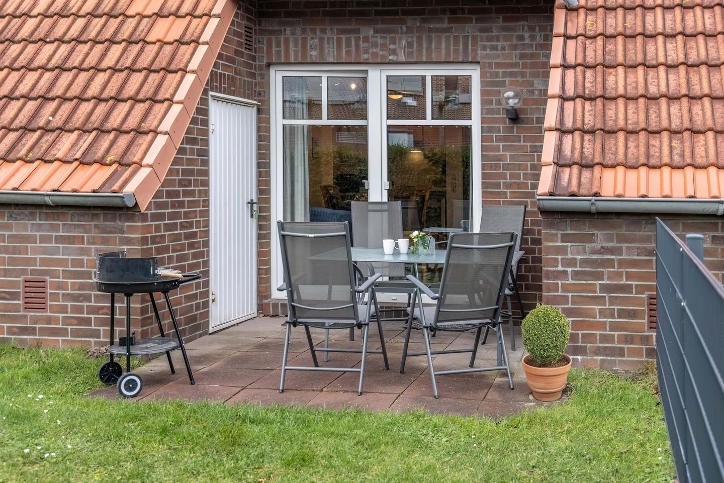 A patio with a table and chairs, a barbecue grill, and a potted plant.