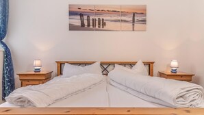 En dobbeltseng med træsengestolpe, to sengeborde med lamper, og et maleri af en solnedgang over havet.
