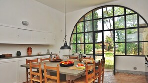 Une cuisine dotée d’une grande fenêtre en arc de cercle, de chaises en bois, d’une table à manger et de divers ustensiles de cuisine.