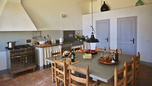 Une cuisine équipée d’une cuisinière, d’un four et d’une table à manger avec des chaises. On y trouve également des placards, un luminaire suspendu et un vase accroché au mur.
