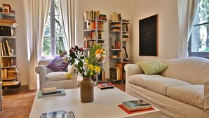 Un salon avec un canapé blanc, une table basse sur laquelle sont posés des livres et un vase de fleurs, et une bibliothèque remplie de livres.