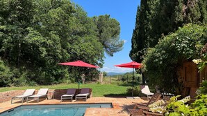 Une piscine entourée de chaises longues et de parasols rouges, le tout agrémenté de verdure et offrant une vue sur des montagnes lointaines.