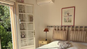 A bedroom with a large bed, a nightstand, a lamp, a window with curtains, and a door leading to a garden. - Dream villa with sea view and private pool in the gulf of Saint-Tropez (Grimaud)