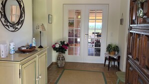A hallway with a mirror, a lamp, a vase with flowers, a wicker basket, and a door leading to a room with a view. - Dream villa with sea view and private pool in the gulf of Saint-Tropez (Grimaud)