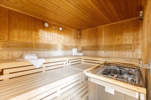 Eine Sauna mit Holzbänken, einem Sitzwärmer und einem steinernen Becken.
