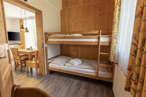 Une chambre avec un lit superposé, un bureau et des chaises en bois, une télévision et une fenêtre avec des rideaux.