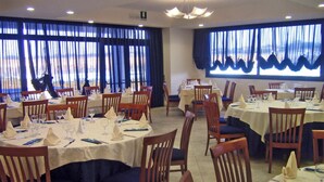 Een restaurant met ronde tafels, stoelen en blauwe gordijnen.